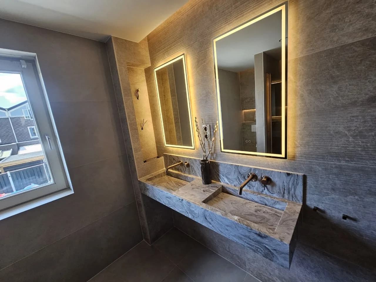 Badkamer met natuursteen wastafel en verlichte spiegels
