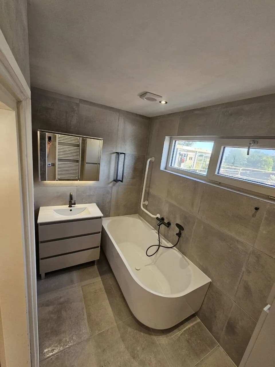 Badkamer met vrijstaand ligbad en grijze tegels