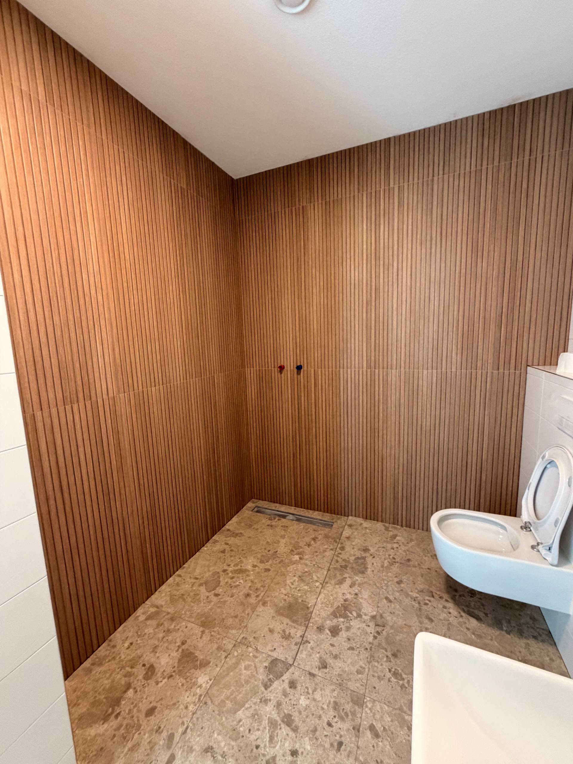 Badkamer met verticale houtlook wandtegels, natuursteen vloertegels en een vlakke douchegoot.