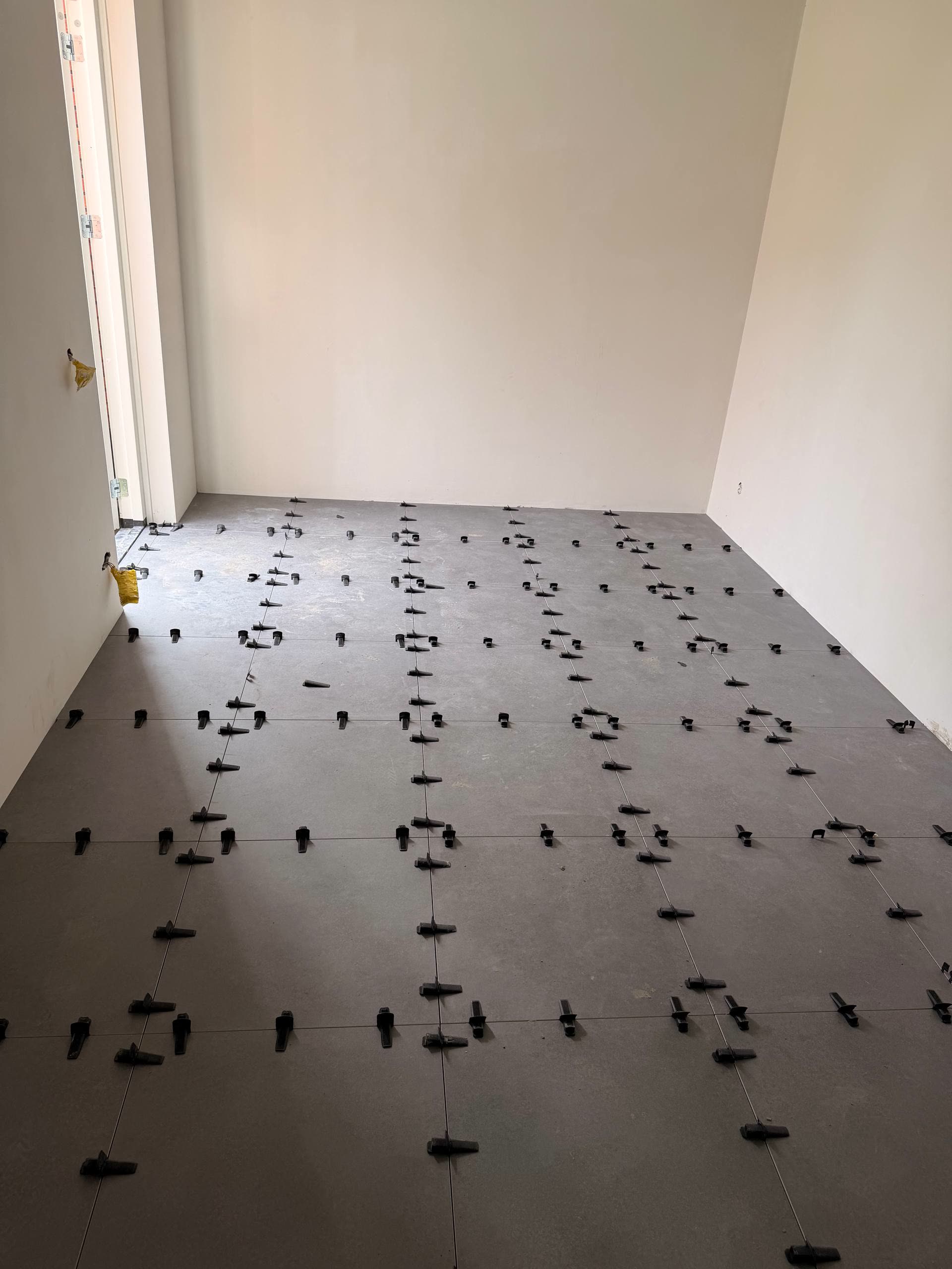 Grootformaat vloertegels in een lege woonkamer, gelegd met nivelleerclips en strakke voeglijnen.