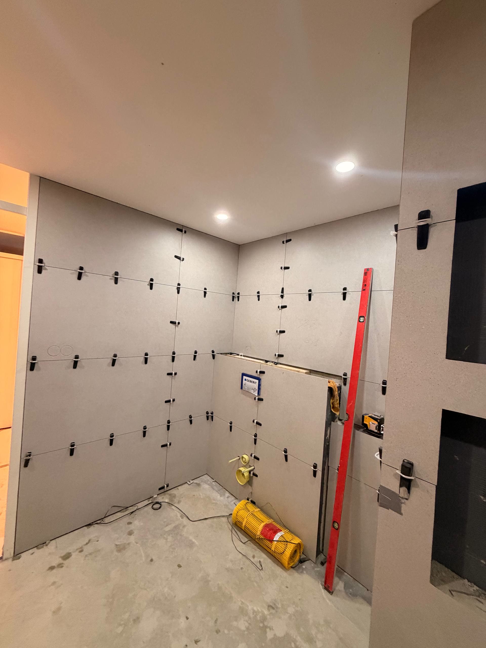 Wandtegels aangebracht met nivelleerclips en een waterpas tegen de wand tijdens het tegelen.